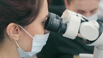 A female doctor looks in a microscope close-up. Side view of female scientist looking into binocular microscope video