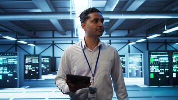 System administrator in data center managing and maintaining databases, ensuring data integrity, security and availability. IT worker updating server room supercomputers systems, camera B video