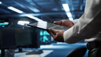 Data center admin responsible for installation of networking systems solving tasks in workspace. Close up of tablet used by IT worker doing maintenance on server farm gear, camera B video
