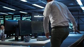 Engineer overseeing data center, making improvements and updates to ensure system can handle networking tasks, handheld camera shot. Indian man in server room tracking network traffic, camera B video