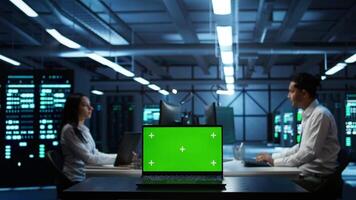 Focus on mockup laptop used by technician in data center in blurry background managing servers. Close up of chroma key notebook used by expert in server hub to ensure networks are secure, camera B video