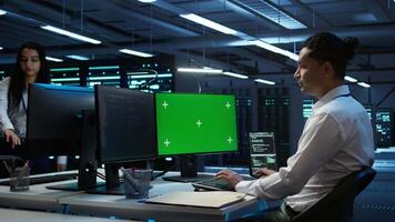 Engineer in data center monitoring security threats using mockup computer, implementing cybersecurity measures. Man using green screen PC, ensuring compliance with regulations, camera B video
