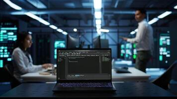 Close up of code running on laptop screen in data center used for managing gear energy consumption. Focus on notebook used by software developer in blurry background in server farm, camera B video
