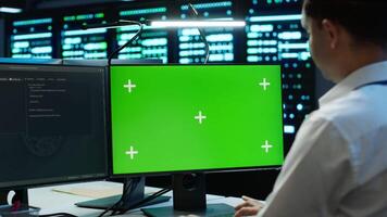 Engineer working with chroma key PC in data center used for managing gear energy consumption. Employee using isolated screen monitor in workspace used for automation in server farm, camera A video