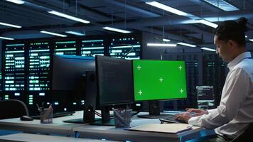 Programmer overseeing data center using isolated screen computer, ensuring system can handle networking tasks. IT expert in server room tracking network traffic with chroma key PC, camera B video