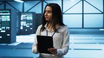Admin in data center monitoring security threats with tablet, implementing cybersecurity measures. Specialist using device, ensuring compliance with regulations to protect data center gear, camera A video