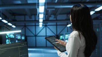 Data center computer scientist designing, implementing and managing infrastructure to ensure optimal performance and reliability. Woman in server room coding on tablet, camera A video
