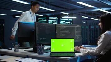 Engineer in high tech data center managing and maintaining databases using mockup devices, ensuring data integrity. Indian employees updating server room supercomputers with chroma key laptop video