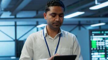 Engineer walking in data center, monitoring security threats, implementing cybersecurity measures. Indian man ensuring compliance with regulations to protect data center gear, camera A video