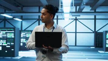 Technician using laptop in data center, managing servers, operating systems. Professional in server hub using notebook to ensure networks are secure and functioning properly, camera A video