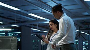 Admins in data center managing and maintaining databases using device, ensuring data integrity and security. IT professionals updating server room workspace systems using tablet video