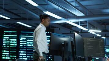 Team of programmers in high tech data center troubleshooting issues using tablet. Teamworking colleagues in server farm using device, establishing performance benchmarks, camera A video