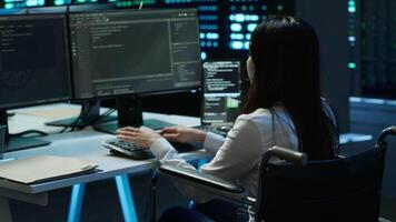 Person with paraplegia in inclusive server hub overseeing data center, making improvements. Woman in wheelchair doing tasks in data center, tracking network traffic, camera A video