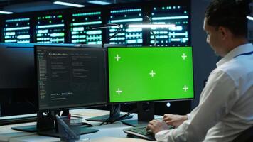 Engineer in data center monitoring security threats using mockup computer, implementing cybersecurity measures. Man using green screen PC, ensuring compliance with regulations, camera A video