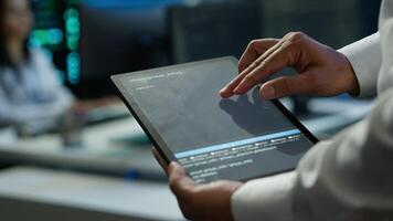 Data center admin responsible for installation of networking systems solving tasks in workspace. Close up of tablet used by IT worker doing maintenance on server farm gear, camera A video
