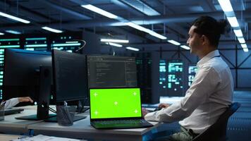 Data center engineer responsible for installation of networking equipment solving tasks on isolated screen laptop. Man doing maintenance on server room infrastructure using mockup notebook, camera B video