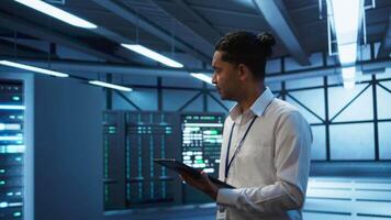 Engineer walking in data center, monitoring security threats, implementing cybersecurity measures. Indian man ensuring compliance with regulations to protect data center gear, camera B video