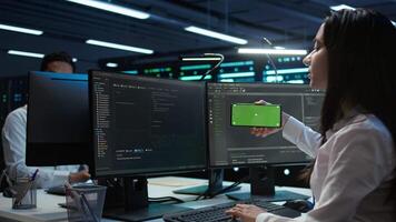 Technician using mockup mobile phone in data center, managing servers. Expert in server hub using isolated screen smartphone to ensure networks are secure and functioning properly, camera B video