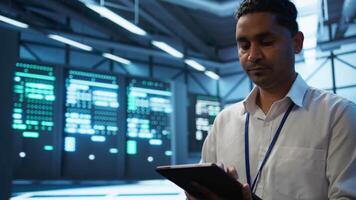 Software developer walking in data center, managing and maintaining databases, ensuring data integrity and security. Close up of man updating server room mainframe systems using tablet, camera B video