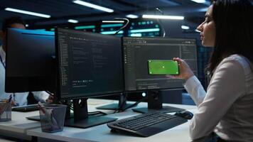 Zoom in on green screen mobile phone used by data center employee troubleshooting issues. Engineer uses mockup smartphone device in server hub, establishing performance benchmarks, camera B video