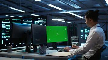 Engineer working with chroma key PC in data center used for managing gear energy consumption. Employee using isolated screen monitor in workspace used for automation in server farm, camera B video