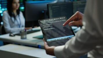 Programmer using device in data center, managing servers, operating systems. Close up of specialist in server hub using tablet to ensure networks are secure and functioning properly, camera A video