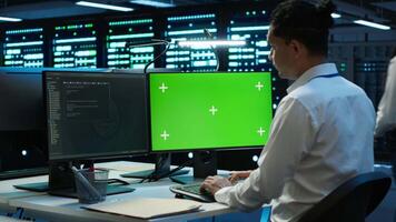 Technician using mockup computer in data center, managing servers, operating systems. Expert in server hub using green screen PC to ensure networks are secure and functioning properly, camera A video
