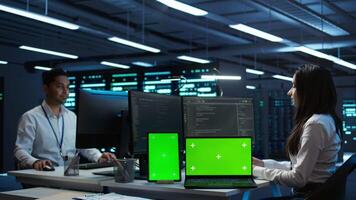 Engineers in data center monitoring security threats using chroma key devices. Experts using isolated screen tablet and laptop, ensuring compliance with regulations, camera B video