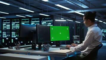 Programmer in data center managing and maintaining databases using mockup PC, ensuring data integrity and security. Expert updating server room systems using green screen computer, camera B video