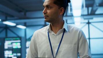 System administrator walks in data center used for managing gear energy consumption, working on tablet. Close up of IT specialist using device in workspace used for automation in server room, camera A video
