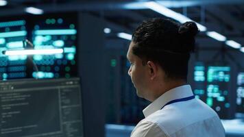 Portrait of smiling technician in data center implementing and managing infrastructure to ensure optimal performance and reliability. Happy IT specialist in server room coding on computer, camera A video