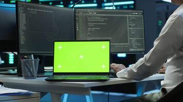 Zoom in on green screen laptop used by data center worker troubleshooting issues. Engineer uses chroma key notebook in server hub, establishing performance benchmarks, camera A video