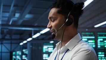 System administrator in data center managing and maintaining databases, ensuring data integrity, security and availability. Indian man updating server farm supercomputers systems, camera B video