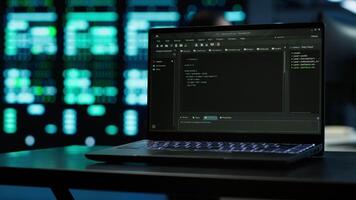 Close up of code running on laptop screen in data center used for managing gear energy consumption. Focus on notebook used by software developer in blurry background in server farm, camera A video