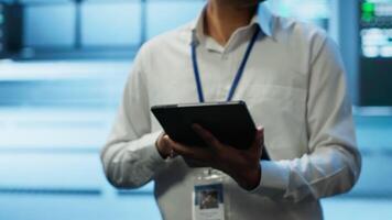 Software developer walking in data center, managing and maintaining databases, ensuring data integrity and security. Close up of man updating server room mainframe systems using tablet, camera A video