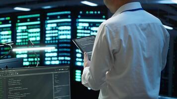 Data center engineer responsible for installation and repair of networking equipment solving tasks on device. IT professional doing maintenance on server room infrastructure using tablet, camera A video