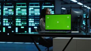Focus on mockup laptop used by technician in data center in blurry background managing servers. Close up of chroma key notebook used by expert in server hub to ensure networks are secure, camera A video