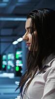 Vertical Computer scientist in data center monitoring security threats using PC, implementing cybersecurity measures. Server farm employee ensuring compliance with regulations, camera B video