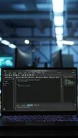 Vertical Close up of code running on laptop screen in data center used for managing gear energy consumption. Focus on notebook used by software developer in blurry background in server farm, camera B video