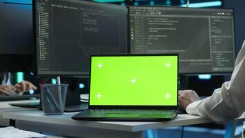 System administrator in data center installing software on isolated screen laptop, troubleshooting issues. Admin uses mockup notebook in server hub, establishing performance benchmarks, camera A video