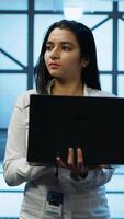 Vertical Programmer walking in data center, using notebook to design, implement and manage gear, ensuring optimal performance and reliability. IT professional in server hub coding on laptop, camera A video