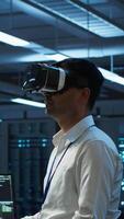 Vertical Engineer wearing VR headset in data center installing software on computer, troubleshooting issues. IT expert in server hub using virtual reality tech, establishing performance benchmarks, camera A video