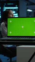 Vertical Focus on mockup laptop used by technician in data center in blurry background managing servers. Close up of chroma key notebook used by expert in server hub to ensure networks are secure, camera A video