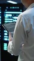 Vertical Data center engineer responsible for installation and repair of networking equipment solving tasks on device. IT professional doing maintenance on server room infrastructure using tablet, camera A video