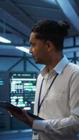 Vertical Engineer walking in data center, monitoring security threats, implementing cybersecurity measures. Indian man ensuring compliance with regulations to protect data center gear, camera B video