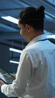 Vertical System administrator overseeing data center, making improvements and updates to ensure system can handle networking tasks. IT expert in server room tracking network traffic with tablet, camera A video