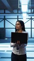 Vertical Programmer walking in data center, using notebook to design, implement and manage gear, ensuring optimal performance and reliability. IT professional in server hub coding on laptop, camera B video