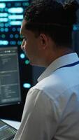 Vertical System administrator in data center installing software on computer, troubleshooting issues using tablet. IT staff member in server hub establishing performance benchmarks, camera A video