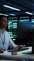 Vertical System administrator in wheelchair overseeing data center using computer, ensuring system can handle networking tasks. Person with paraplegia in server room tracking network traffic with PC video