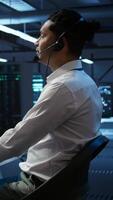 Vertical Data center computer scientist wearing mic headset, doing installation of networking equipment. Server hub IT professional talking in microphone with system administrators, camera B video